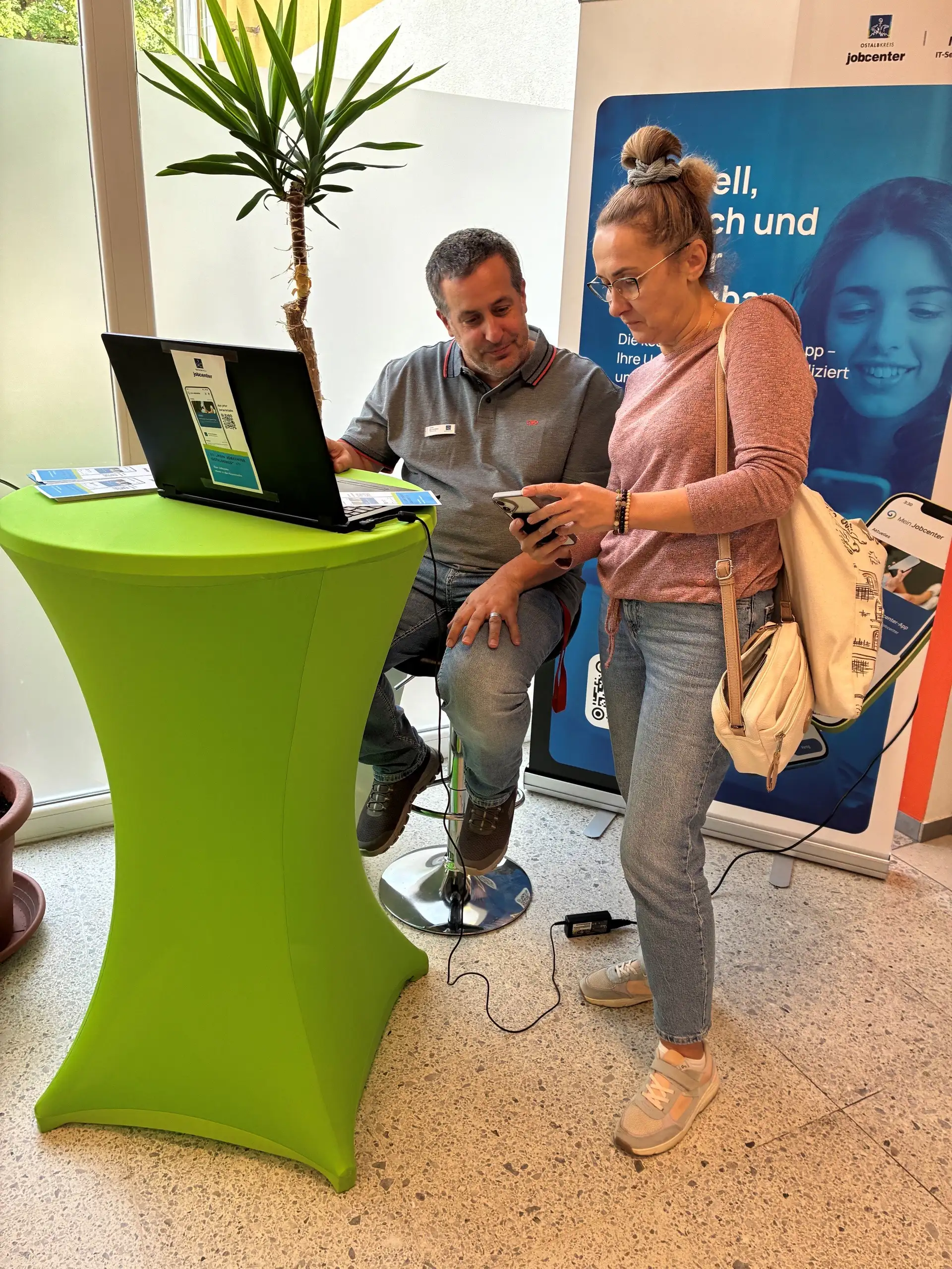 Integrationsberater Christian Bechstein (links) unterstützt eine Kundin bei der Einrichtung und Personalisierung der Jobcenter-App. Seite 2/1