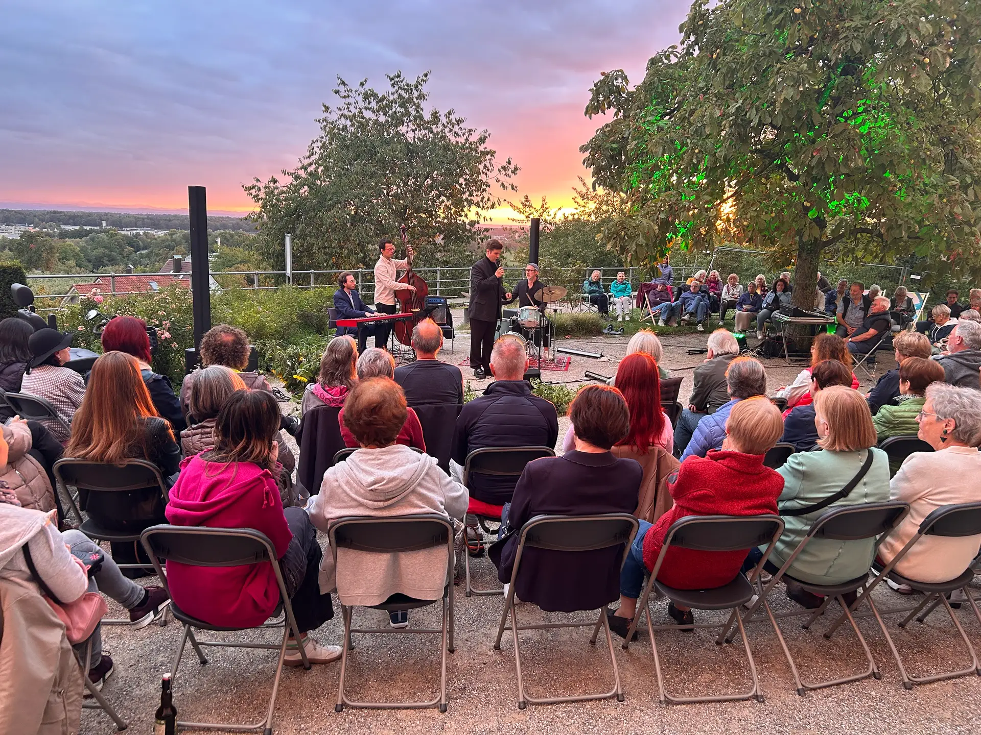 Musiker spielt Gitarre bei Abendkonzert auf der Open-Air-Bühne, im Hintergrund eine größere Gruppe von Zuschauern.