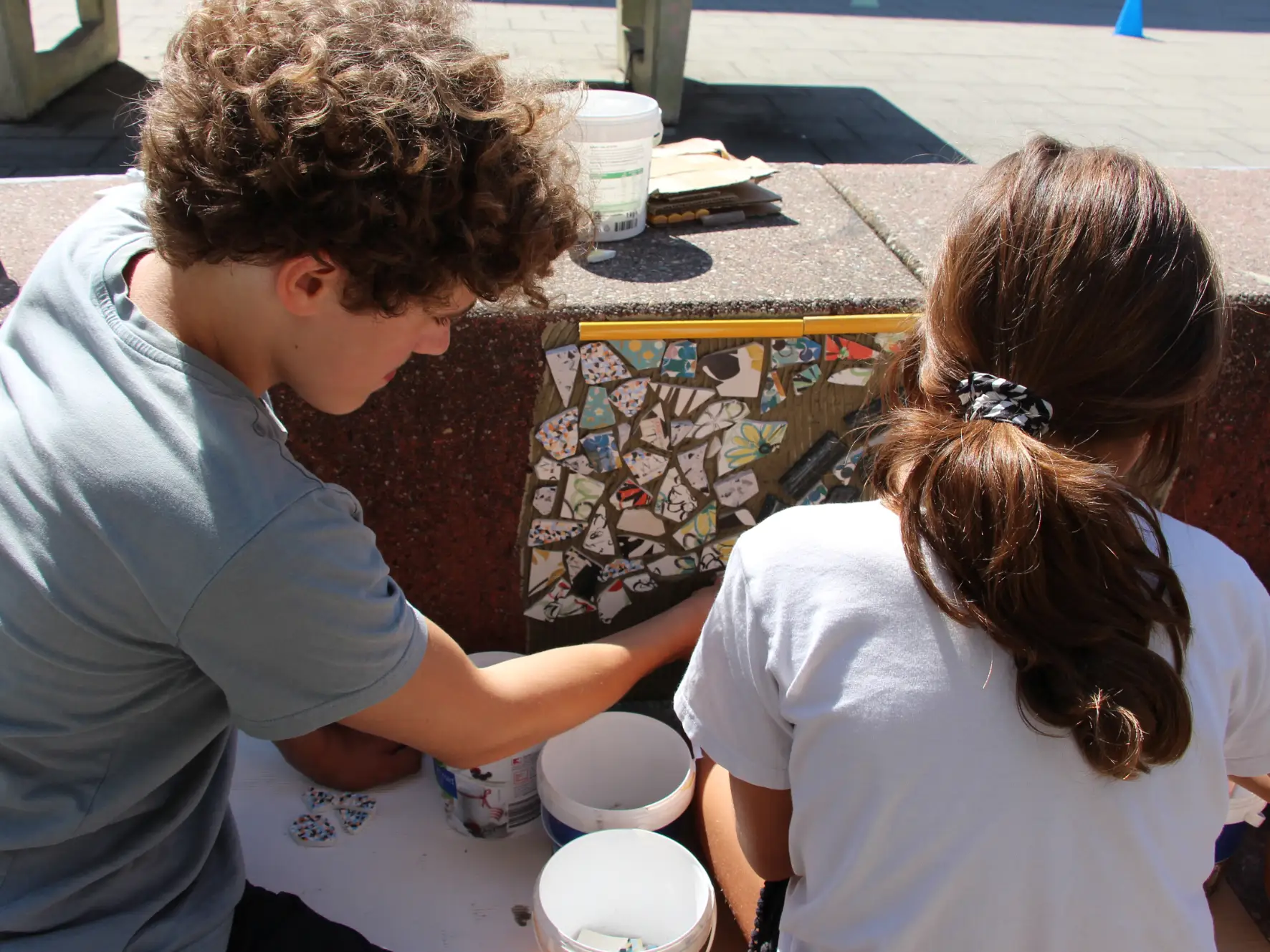 Kinder gestalten im Hof des Spielehauses ein Mosaikprojekt aus bunten Fliesenresten.
