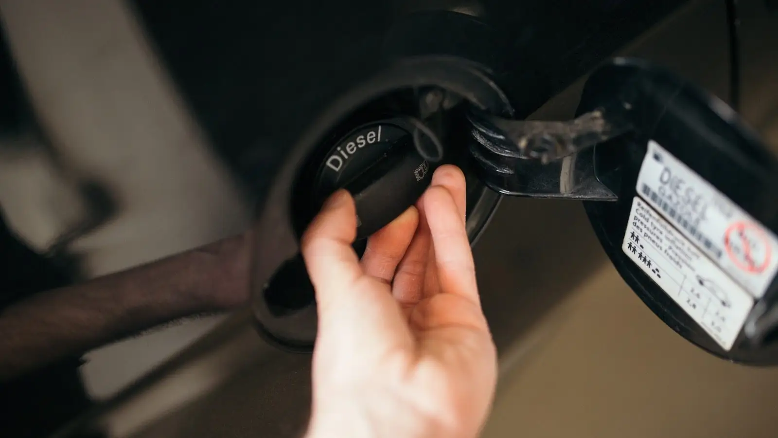Eine Hand öffnet den mit Diesel beschrifteten Tankverschluss eines Autos.